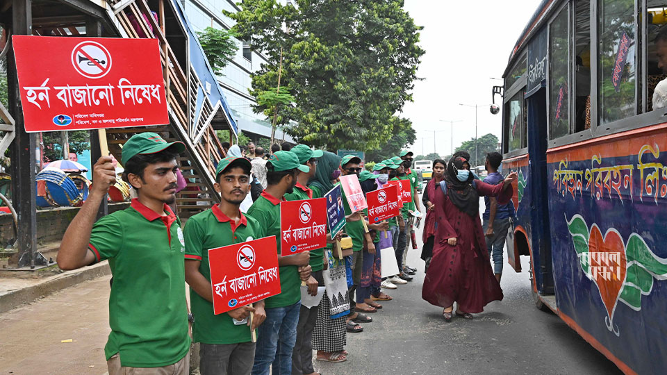 যেখানে এসে বাস থামে, সেখানে ‘হর্ন বাজানো নিষেধ’ লেখা প্ল্যাকার্ড হাতে দাঁড়িয়ে আছেন স্বেচ্ছাসেবীরা। ছবি : সকাল সন্ধ্যা